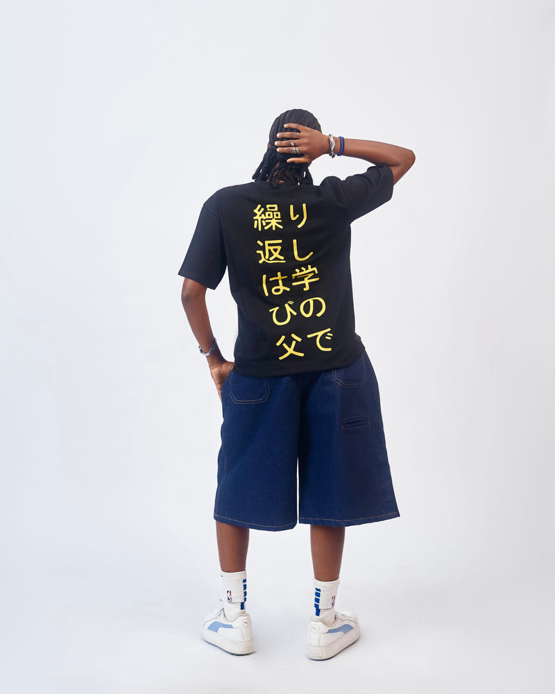 Back view of a model wearing the black T-shirt with yellow Japanese text and navy denim shorts
