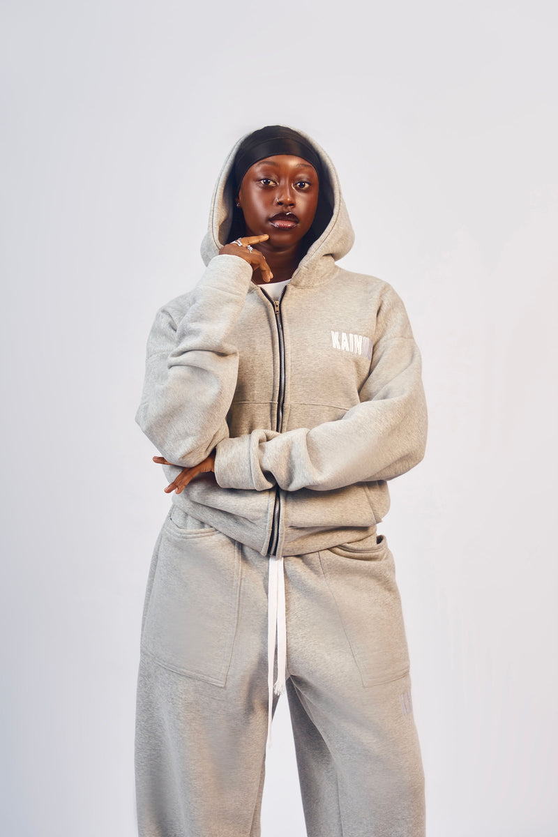 Model wearing the light grey zip-up hoodie with the hood up and matching sweatpants